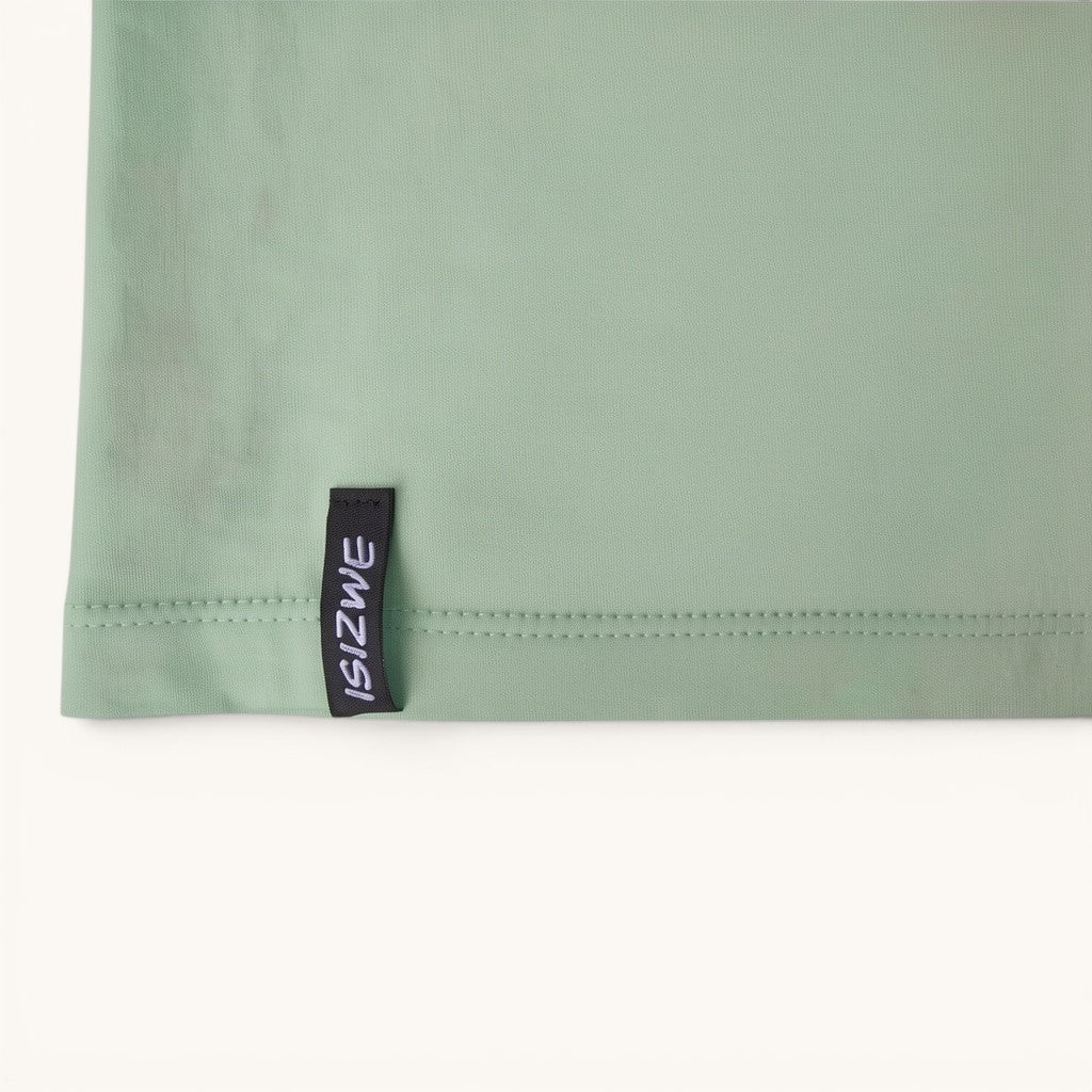 Camiseta ISIZWE verde salvia de algodón orgánico con etiqueta gráfica en la costura inferior.